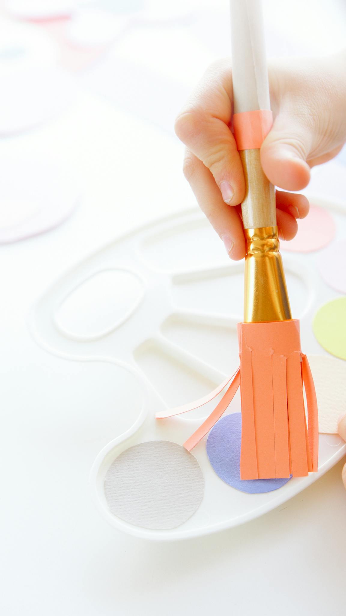 Close-up of a child holding a paintbrush over a colorful palette indoors.