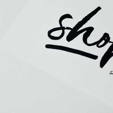 Elegant handwritten 'shop' sign on white background, perfect for retail design.